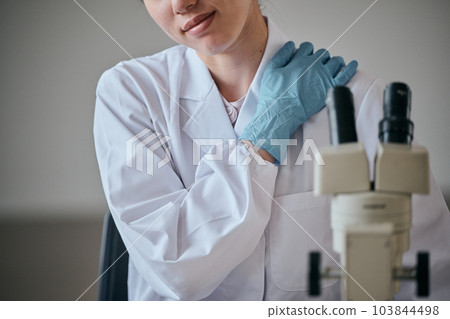 一位身穿白大褂的年輕女子雙手托著僵硬的肩膀 一位身穿白大褂的年輕女子雙手托著僵硬的肩膀 103844498