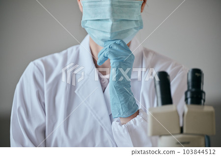 一位身穿白大衣的年輕女子在辦公桌前用手托著下巴思考 103844512