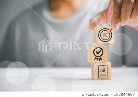 Hand displaying a wooden block cube with an icon, representing company strategy development. Conceptual image of success and business goals. Hand displaying a wooden block cube with an icon, representing company strategy development. Conceptual image of success and business goals. 103844667
