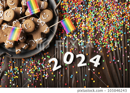 New year background of tray with gingerbread cookie men, rainbow flags and color sprinkles on wooden table 103846243