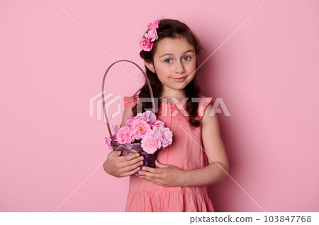 Kids fashion concept. Elegant sweet little girl wearing hairstyle with roses and elegant romantic pink dress, posing with basket of beautiful flowers, isolated background. Happy Women's Day. Children Kids fashion concept. Elegant sweet little girl wearing hairstyle with roses and elegant romantic pink dress, posing with basket of beautiful flowers, isolated background. Happy Women's Day. Children 103847768