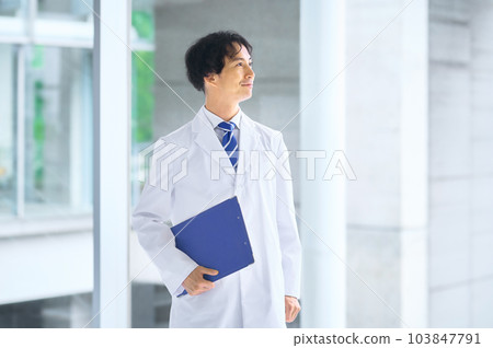 A young male doctor in a lab coat standing in the hospital corridor A young male doctor in a lab coat standing in the hospital corridor 103847791