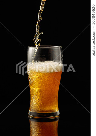 Pouring beer into a glass on a black reflective background. Pouring beer into a glass on a black reflective background. 103849620