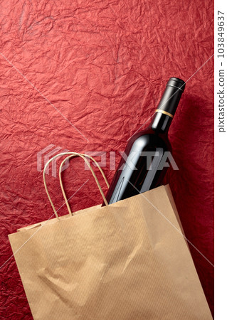 Paper shopping bag with a bottle of red wine on a textured red background. Paper shopping bag with a bottle of red wine on a textured red background. 103849637