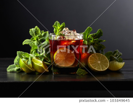 Cocktail Cuba Libre with rum, cola, mint, and lime on a black background. Cocktail Cuba Libre with rum, cola, mint, and lime on a black background. 103849645