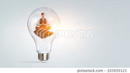 Businessman doing yoga in lotus pose inside light bulb 103850121
