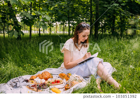 Beautiful woman on picnic. She smiles, eats strawberries and enjoys summer. 103851392