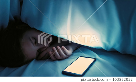 Child obsession. Technology addiction. Night social media. Girl fell asleep with white unlocked smartphone blank mockup screen in dark bedroom at home empty space. 103852032
