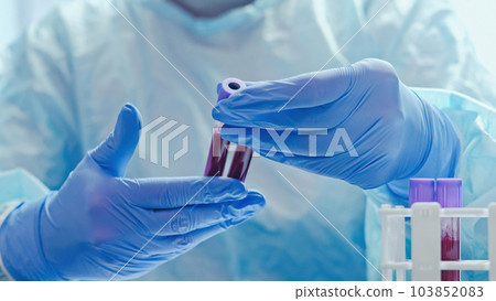 Blood diagnostics. Laboratory analysis. Microbiology test. Medical worker with hands in protective rubber gloves studying examining samples tubes. 103852083