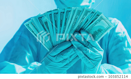 Healthcare costs. Medical expenses. Doctor salary. Surgeon hands in protective equipment holding US dollar cash money fan on blue gradient background. 103852114