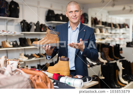 Male sales consultant offering demi-season mens boots in shoe store 103853879