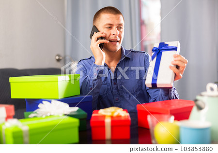 Happy man sitting with many presents, using phone 103853880