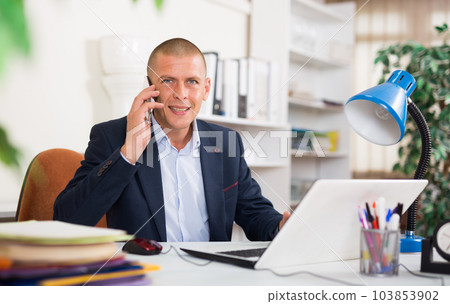 Manager sitting at office table, having phone conversation 103853902