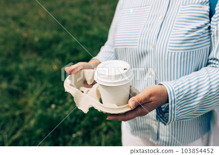 Womans hands hold coffee in coffee paper cup on nature background. Close up. 103854452