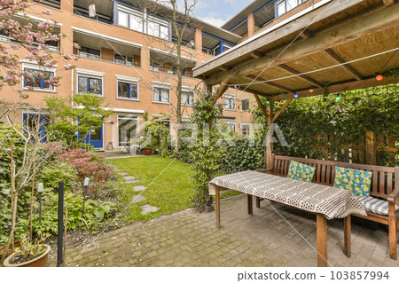 an outside area with a table and bench in the middle, surrounded by plants and trees on either side of the building an outside area with a table and bench in the middle, surrounded by plants and trees on either side of the building 103857994