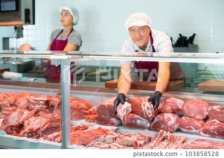 Elderly male seller shows demonstrates raw beef ribs in glass showcase of refrigerator Elderly male seller shows demonstrates raw beef ribs in glass showcase of refrigerator 103858528