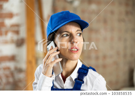 Woman builder using smartphone while standing in renovated room Woman builder using smartphone while standing in renovated room 103858535