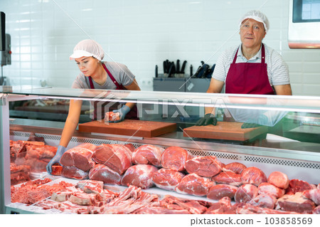 Elderly butcher shop owner standing behind display case with meat Elderly butcher shop owner standing behind display case with meat 103858569
