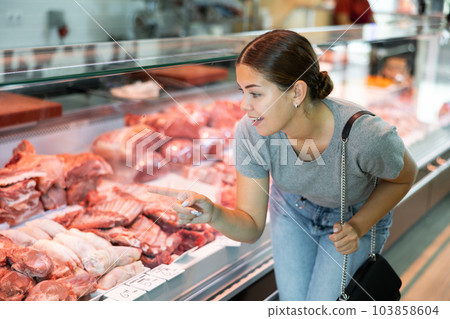 Customer girl looks at glass display case of refrigerator and chooses pork wing ribs 103858604