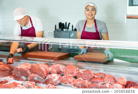 In butcher shop, young female vendor in uniform apron, gloves, cap holds cutting board 103858838