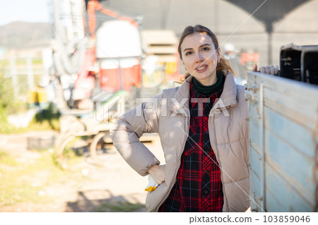 Smiling young female farmer standing in backyard of farm leaning on truck Smiling young female farmer standing in backyard of farm leaning on truck 103859046
