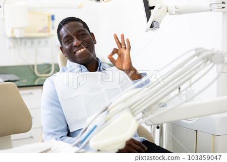 Portrait of positive man making ok gesture, sitting on dental chair Portrait of positive man making ok gesture, sitting on dental chair 103859047