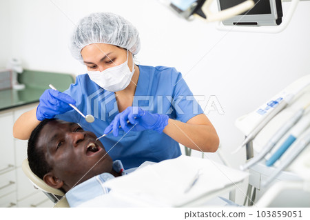Focused female dentist with patient during teeth treatment in dental office Focused female dentist with patient during teeth treatment in dental office 103859051