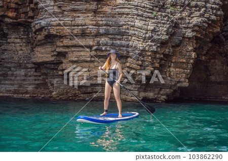 Young women Having Fun Stand Up Paddling in blue water seaamong the rocks in Montenegro. SUP 103862290