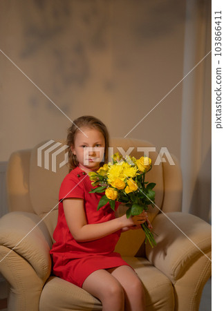 An elegant girl in a red dress with a bouquet of yellow roses sits in an armchair. Retro style. 103866411