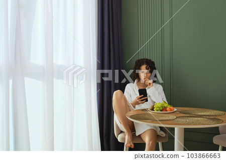 Woman in bathrobe using smartphone and eats grapes after taking bath Woman in bathrobe using smartphone and eats grapes after taking bath 103866663
