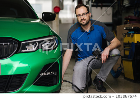 Man inflates the tires on auto service. Mechanic in glasses inspection the car at garage 103867674