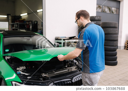 Man auto mechanic closes the hood of the car after inspection 103867688