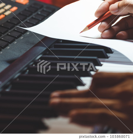 close up songwriter hand writing a hit song on music sheet while playing piano. song writing concept close up songwriter hand writing a hit song on music sheet while playing piano. song writing concept 103868071