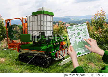 Farmer controls autonomous robot sprayer in a fruit garden. 103869123
