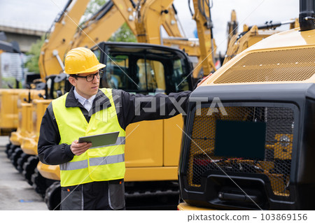 Engineer with a digital tablet stands next to construction excavators 103869156