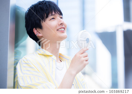 A young man cooling off with a portable fan A young man cooling off with a portable fan 103869217