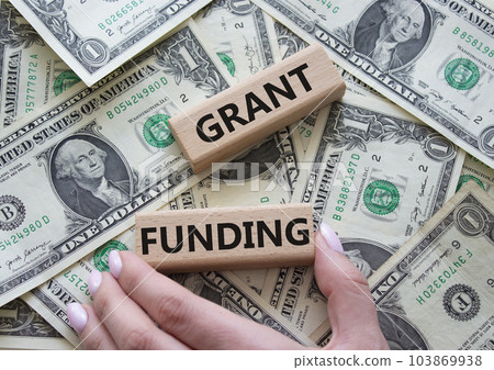 Grant funding symbol. Wooden blocks with words Grant funding. Beautiful dollar background. Businessman hand. Business and Grant funding concept. Copy space. Grant funding symbol. Wooden blocks with words Grant funding. Beautiful dollar background. Businessman hand. Business and Grant funding concept. Copy space. 103869938