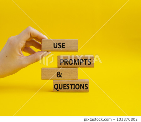 Prompts and Questions symbol. Concept word. Use Prompts and Questions on wooden blocks. Beautiful yellow background. Businessman hand. Business and Prompts and Questions concept. Copy space 103870802
