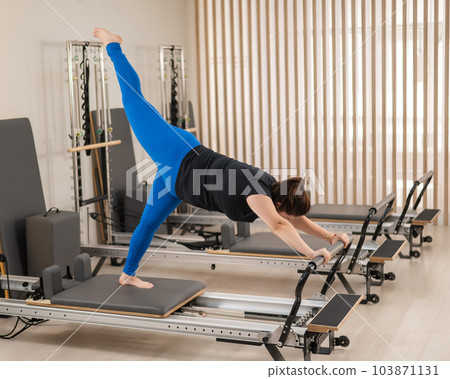 Overweight caucasian woman doing pilates exercises on a reformer. Overweight caucasian woman doing pilates exercises on a reformer. 103871131