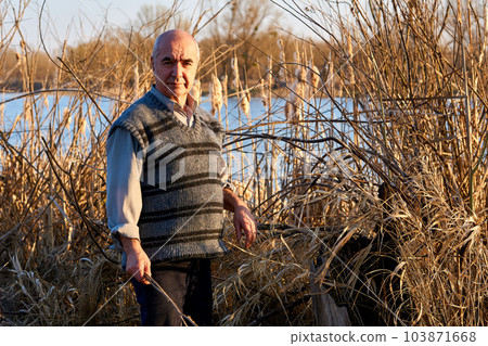 Elderly cheerful pensioner in a picnic in nature among the reeds on the lake Elderly cheerful pensioner in a picnic in nature among the reeds on the lake 103871668