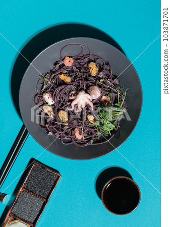 Seafood black pasta served with microgreens. Top view on a blue background, with gravy boats and chopsticks. Seafood black pasta served with microgreens. Top view on a blue background, with gravy boats and chopsticks. 103871701