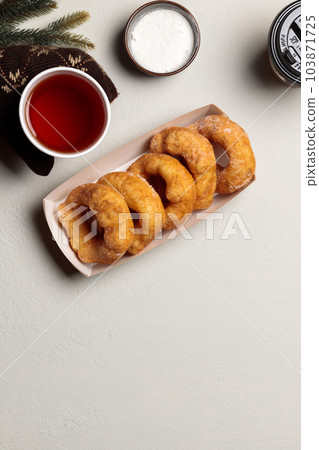 mittened hands hold a cardboard plate with donuts. Flatlay on a light background, with a hot drink and fir branches. Vertical mittened hands hold a cardboard plate with donuts. Flatlay on a light background, with a hot drink and fir branches. Vertical 103871725
