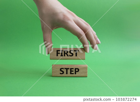 First step symbol. Wooden blocks with words 'First step'. Beautiful green background. Businessman hand. Business and 'First step' concept. Copy space. First step symbol. Wooden blocks with words 'First step'. Beautiful green background. Businessman hand. Business and 'First step' concept. Copy space. 103872274