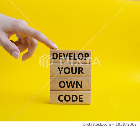 Develop your own code symbol. Concept words Develop your own code on wooden blocks. Beautiful yellow background. Businessman hand. Business and Develop your own code concept. Copy space. 103872362