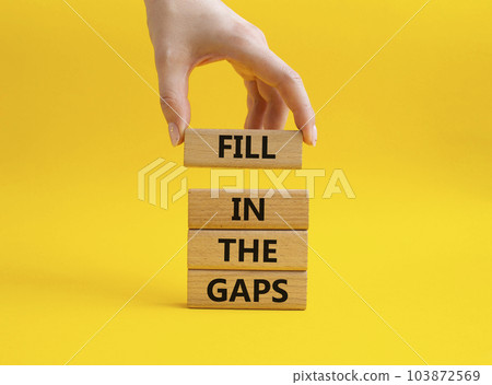 Fill in the gaps symbol. Concept words fill in the gaps on wooden blocks. Beautiful yellow background. Businessman hand. Business and fill in the gaps concept. Copy space. 103872569