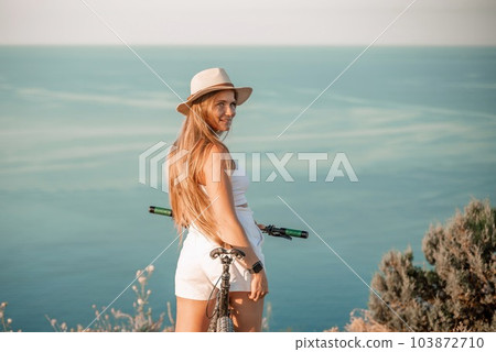 A woman cyclist on a mountain bike looking at the landscape sea. Adventure travel on bike. 103872710