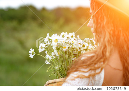 A middle-aged woman in a white dress and brown hat holds a large bouquet of daisies in her hands. Wildflowers for congratulations 103872849