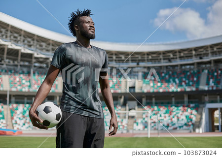 A young man stands in a stadium with a soccer ball in his hand 103873024