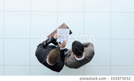 Two businessman signing an agreement. One hand holds the document and the other signs. 103873032