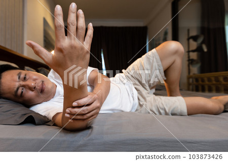 Asian middle-aged man having numbness in hand and wrist from slept on top of his arm, male people massaging his arm and hand from beriberi while lying on bed,health care,medical,lifestyle concept 103873426